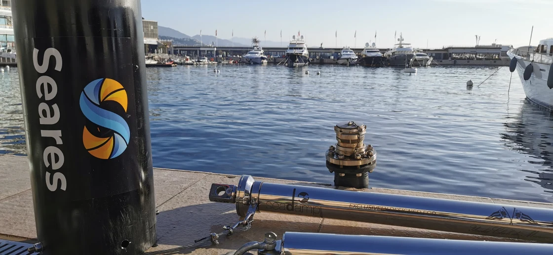 Ammortizzatori di ormeggio in acciaio Seadamp sul molo dello Yacht Club de Monaco, accanto a un cilindro nero con il logo Seares. Sullo sfondo, yacht ormeggiati nel porto